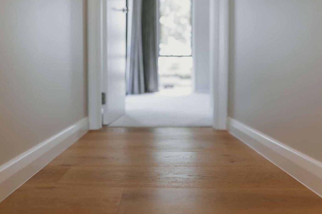Timber-look bedroom flooring in a light-filled hallway leading into a modern bedroom, showing a clean and durable timber-style finish.